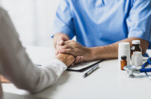 A doctor is holding the hand of a patient and comforting them during a mental illness assessment.