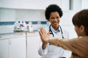 A young girl gives her pediatrician a high five during her pediatric appointment with her parent.