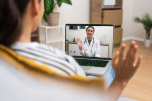 A young woman is having a friendly video call with her doctor, who is providing telehealth primary care medical services.