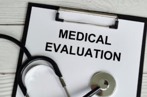 Medical evaluation notes written on a white paper clipboard, accompanied by a stethoscope on a wooden table background.