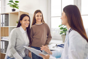 Image of of a teenager girl patient with her mother talking with paediatrician doctor in clinic.